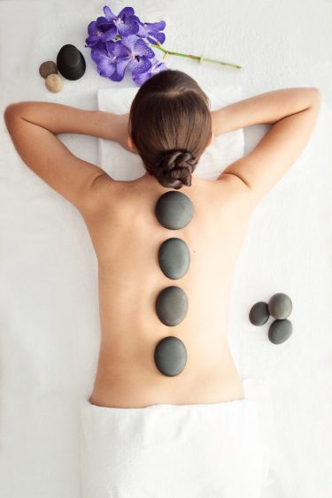 Stone treatment. Top view of beautiful young woman lying on front with spa stones on her back.  Beauty treatment concept.